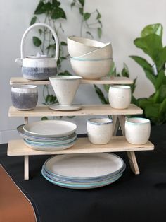 a table with plates and bowls on it, next to a potted plant in the background