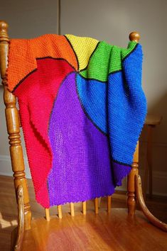 a wooden rocking chair with a multicolored blanket on it's back and legs