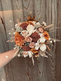 a person holding a bouquet of flowers in front of a wooden wall with planks