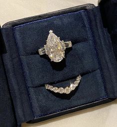 an open ring box with two wedding bands and a pear shaped diamond in it's center