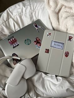 two laptops sitting on top of a white bed covered in blankets and pillows with stickers