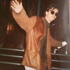 a man in brown jacket and sunglasses waving