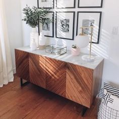 a wooden cabinet with pictures on the wall above it and a plant next to it