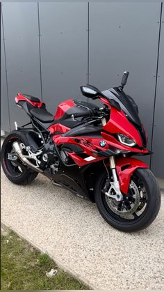 a red and black motorcycle parked in front of a gray wall on the side of a road