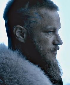 a man with tattoos on his face and beard is looking off to the side while wearing a fur coat