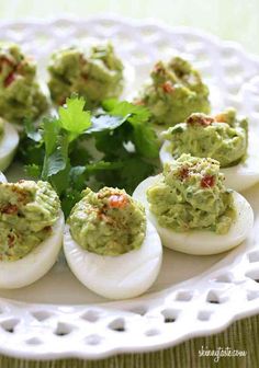 deviled eggs topped with guacamole and cilantro on a white plate