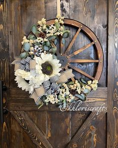 a wreath with white flowers and greenery is hanging on a wooden door that has a wagon wheel