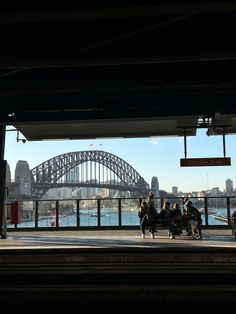 some people are riding on motorcycles by the water and a large bridge in the background