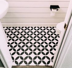 a white toilet sitting next to a black and white tiled floor in a bathroom under a faucet