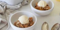 two bowls filled with dessert sitting on top of a table next to silver spoons