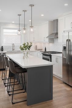 a kitchen with white cabinets and stainless steel appliances in the center, along with bar stools