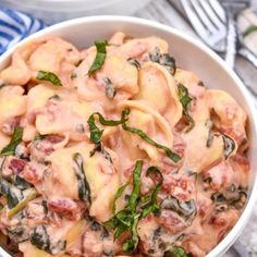 a white bowl filled with pasta and spinach covered in sauce on top of a table