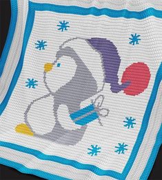 a cross stitch blanket with a penguin holding a ball on it's back, and snowflakes in the background