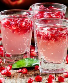 three glasses filled with pomegranate on top of a wooden table