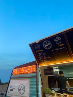 there is a man standing at the counter in front of a food truck that has burgers on it