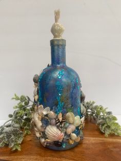 a blue glass bottle with shells and seaweed on it sitting on top of a wooden table