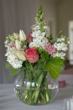 a vase filled with lots of flowers on top of a white tablecloth covered table