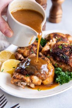 someone pouring gravy onto some chicken on a plate