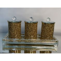 three gold glitter canisters sitting on top of a glass shelf