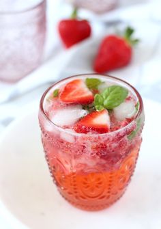 a glass filled with ice and strawberries on top of a white plate