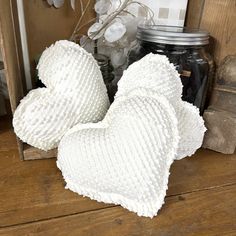 two white heart shaped pillows sitting on top of a wooden table next to jars and flowers