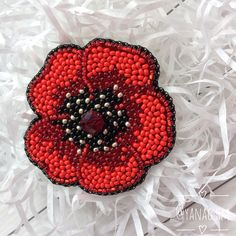 a red and black beaded poppy flower brooch on white shredded paper with beads