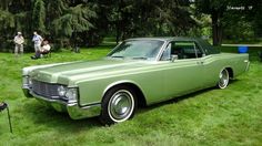 an old green car is parked in the grass with people standing around it and onlookers