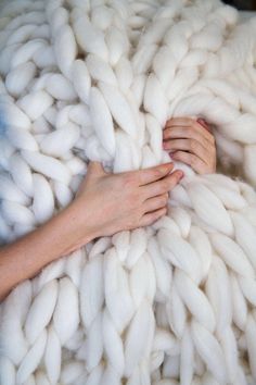 two hands are touching the ends of a large chunky white blanket that is being held by someone's hand