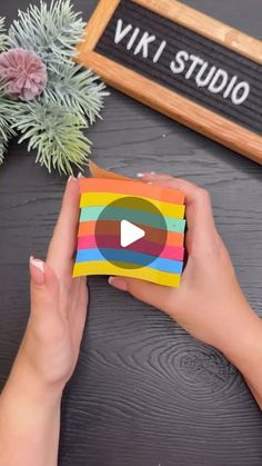 someone holding up a colorful sticker on top of a wooden table next to plants