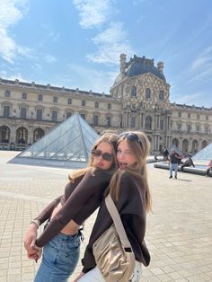 two young women standing next to each other in front of a building with a pyramid