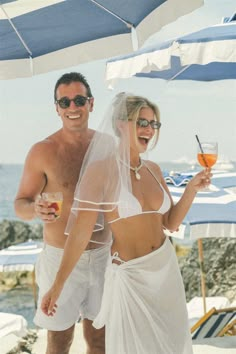 a man and woman standing next to each other under an umbrella with drinks in their hands