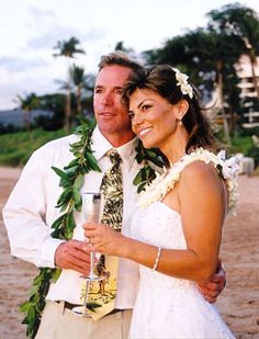 a man and woman standing next to each other on a beach with palm trees in the background