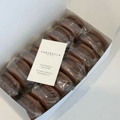 a box filled with chocolate covered cookies on top of a white countertop next to a paper sign