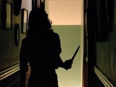 the silhouette of a person holding a knife in their hand while walking down a hallway