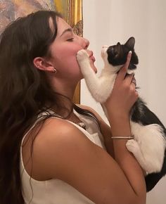 a woman holding a black and white cat up to her face in front of a mirror