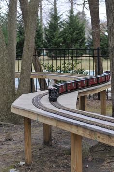 a toy train is coming down the track near some trees and fenced in area