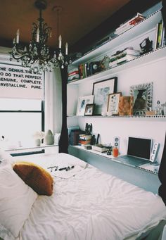 a white bed sitting under a chandelier in a bedroom next to a window