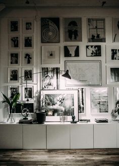 a room filled with lots of framed pictures and plants on top of a shelf next to a lamp