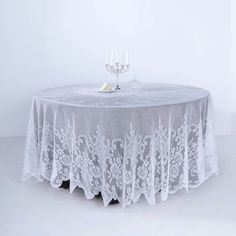 the table is covered with white lace and has two wine glasses on top of it