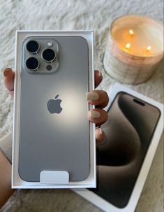 a person holding an iphone in their hand with the box open next to it and a lit candle