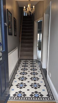 a hallway with stairs and tiled flooring next to a chandelier hanging from the ceiling