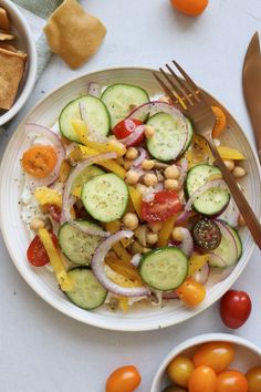 a white plate topped with cucumbers, tomatoes and other vegetables next to chips