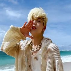 a young man standing on top of a beach next to the ocean holding his hand up