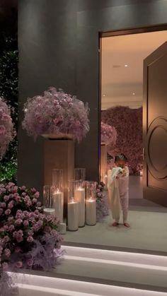 a woman standing in front of a doorway with candles and flowers on the steps next to her