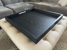 a black tray sitting on top of a white ottoman in front of a gray couch