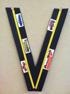 the letter v is made out of black and yellow ribbon with cars on it's sides