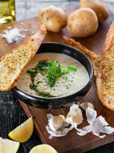 a bowl of soup with bread and garlic on a cutting board