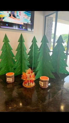 there are three small christmas trees on the table with cups and candy in front of them