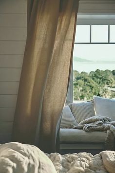 a white couch sitting in front of a window next to a blanket on top of a bed