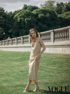 a woman standing in the grass with her hands on her hips and looking at the camera